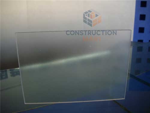 Frosted polycarbonate sheet placed vertically on a glass table, photographed through the matte side to show soft light diffusion, perfect for bathroom privacy screens.